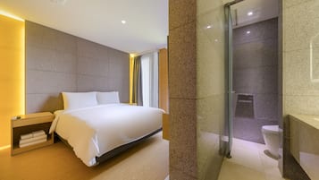A modern hotel room with a large bed, bedside tables, a glass shower enclosure, and a visible toilet.