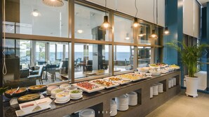 Montaje de bufé con diversos alimentos y vista al mar a través de amplias ventanas.