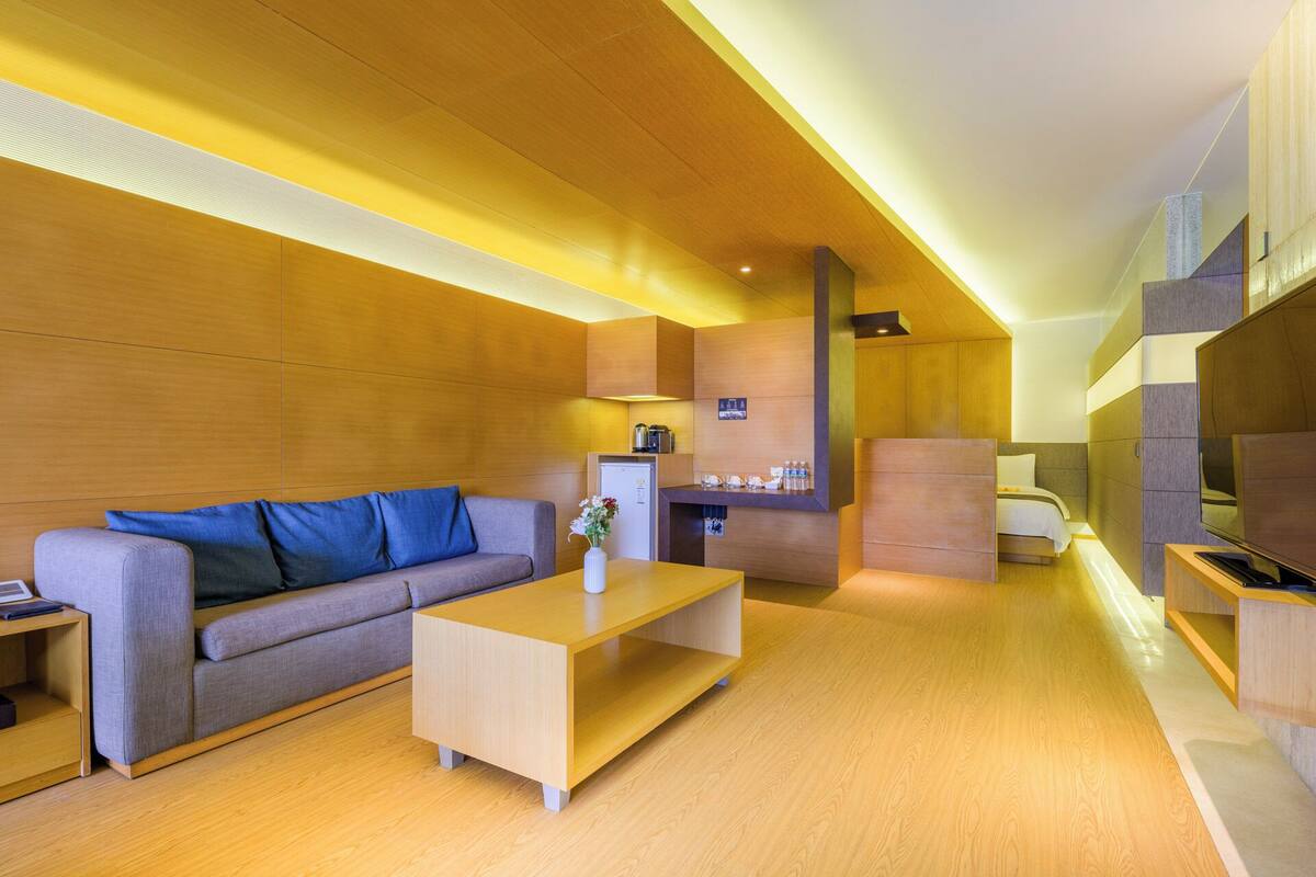 A modern hotel room with a sofa, a coffee table, a desk, a bed, and a TV.