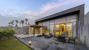 Una casa moderna con patio, mobiliario exterior y palmeras.