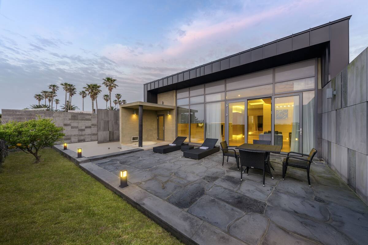 A modern house with a patio, outdoor seating, and palm trees.