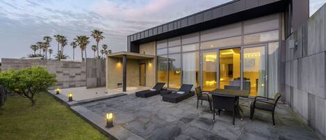 A modern house with a patio, outdoor seating, and palm trees.