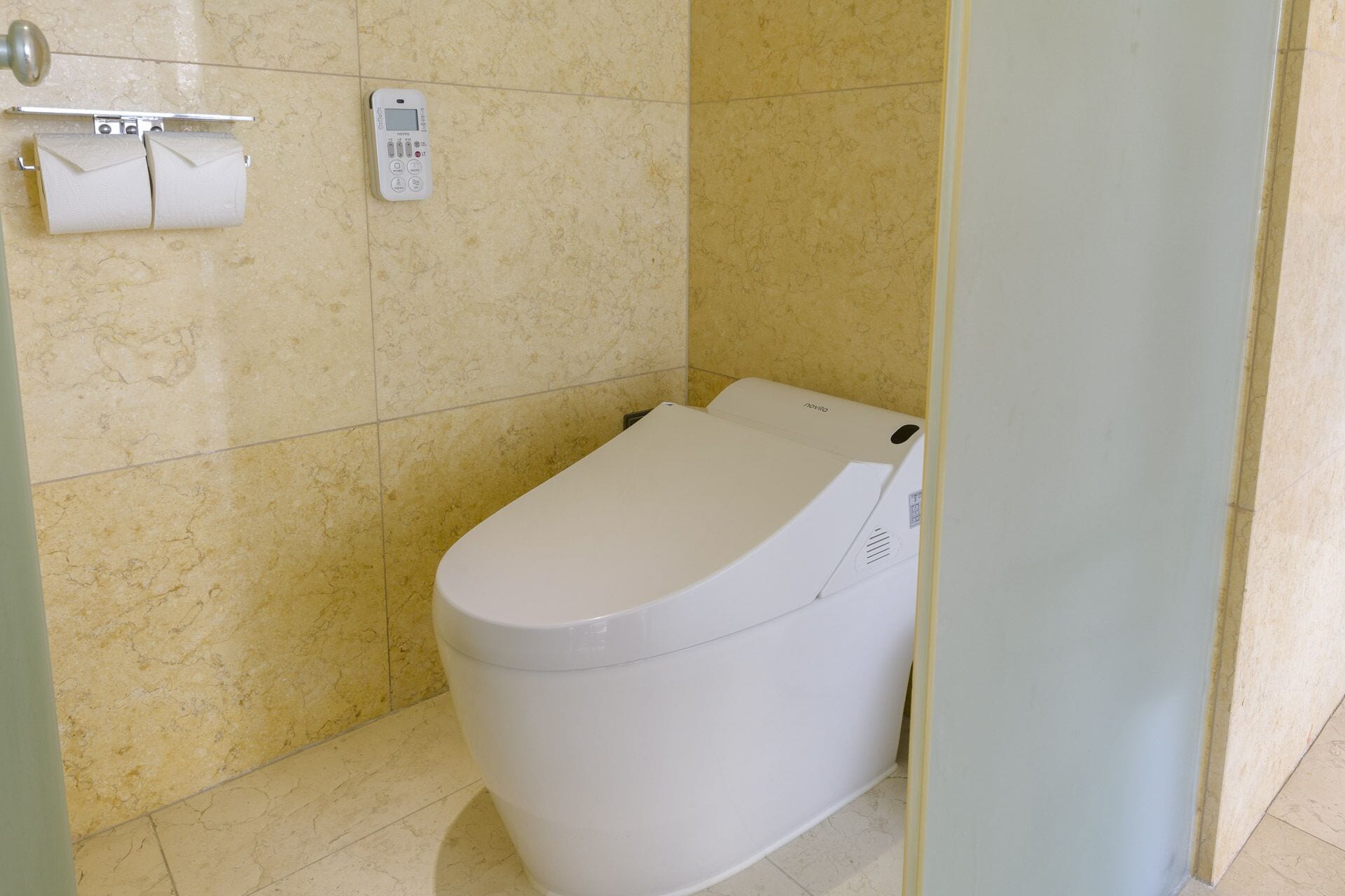 A bathroom with a toilet, a toilet paper holder, and a wall-mounted control panel.
