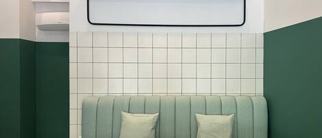 A restaurant interior with a wooden table, green cushioned seating, a tiled wall, and a geometric wall art piece.