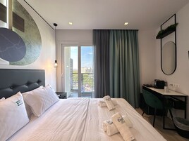 Una habitación de hotel con cama, escritorio, silla y un ventanal con cortinas.