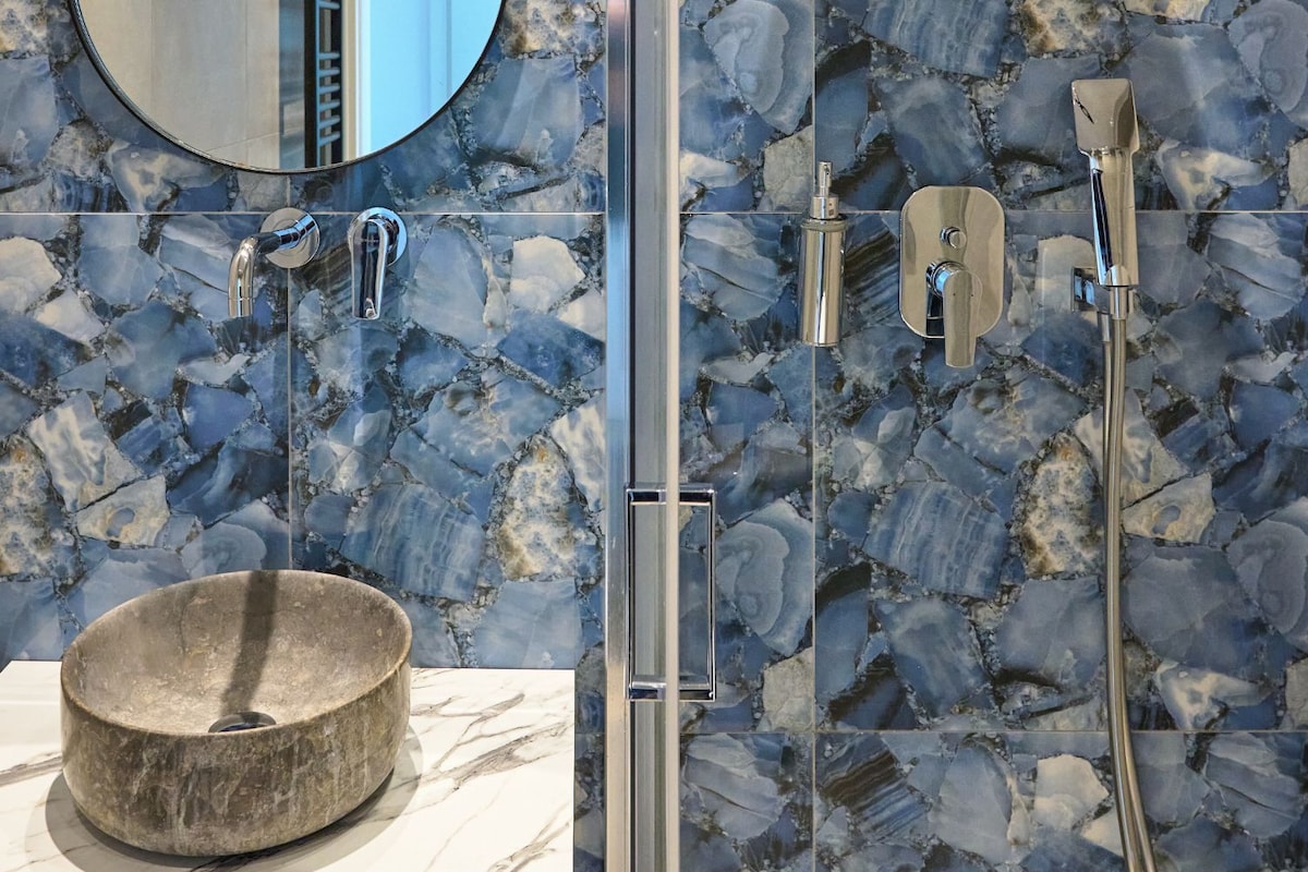 Ein Badezimmer mit einem runden Spiegel, einem Waschbecken und einer Dusche mit Regendusche.