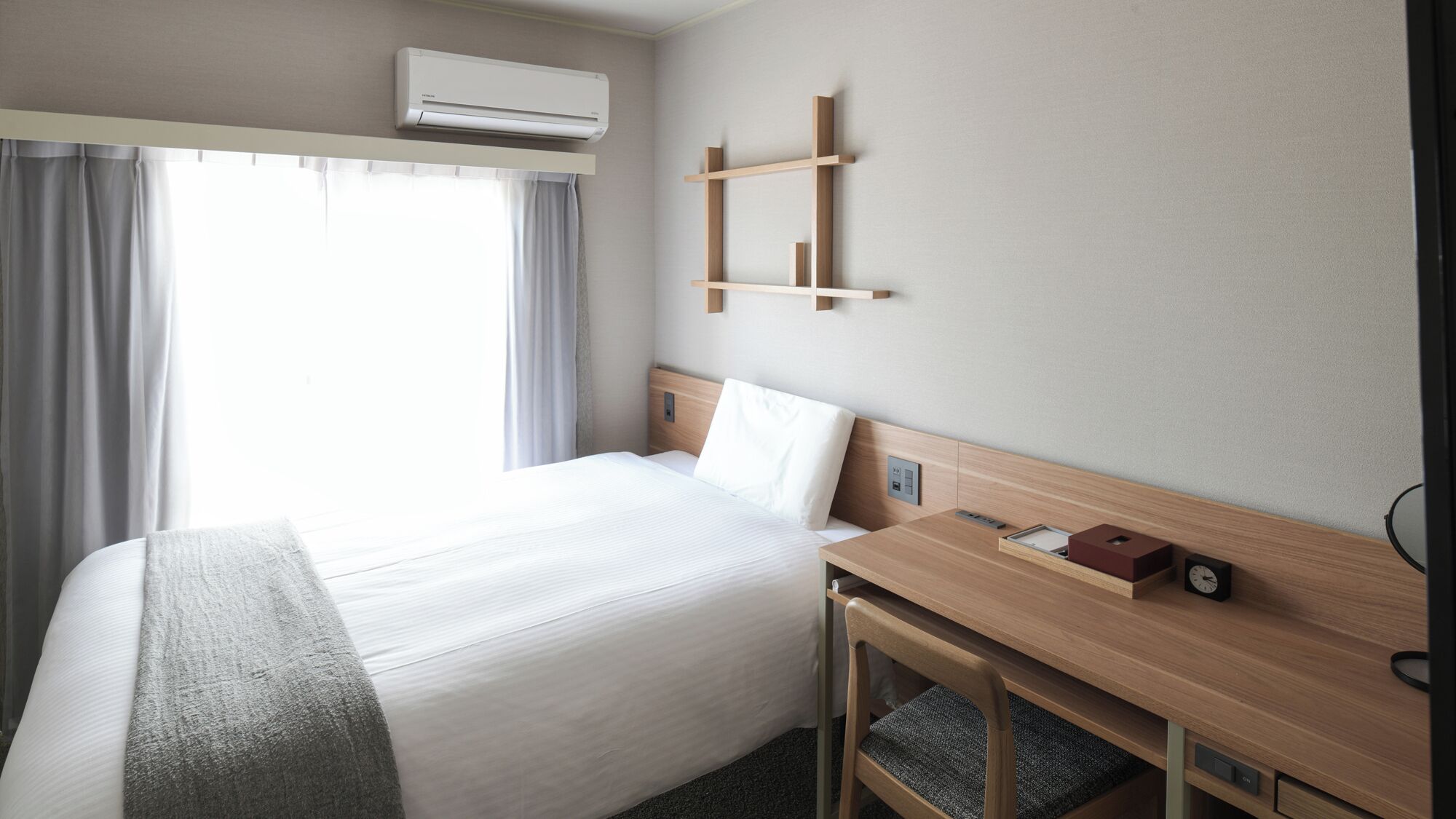 A hotel room with a bed, bedside table, and a wall-mounted shelf.