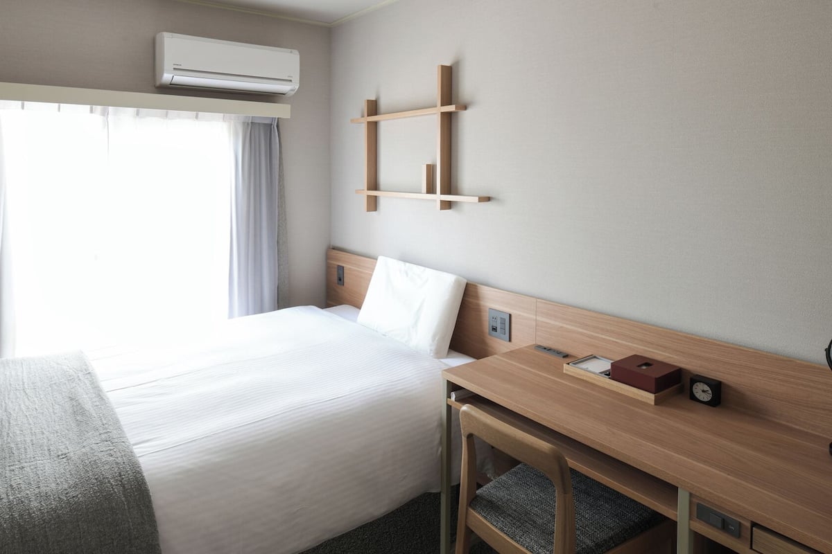 A hotel room with a bed, bedside table, and a wall-mounted shelf.