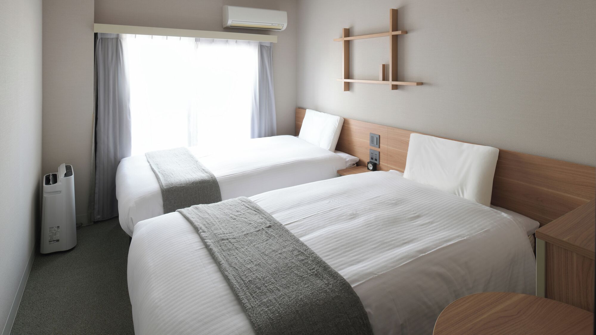 A hotel room with two beds, a bedside table, a wall-mounted shelf, and a window with curtains.