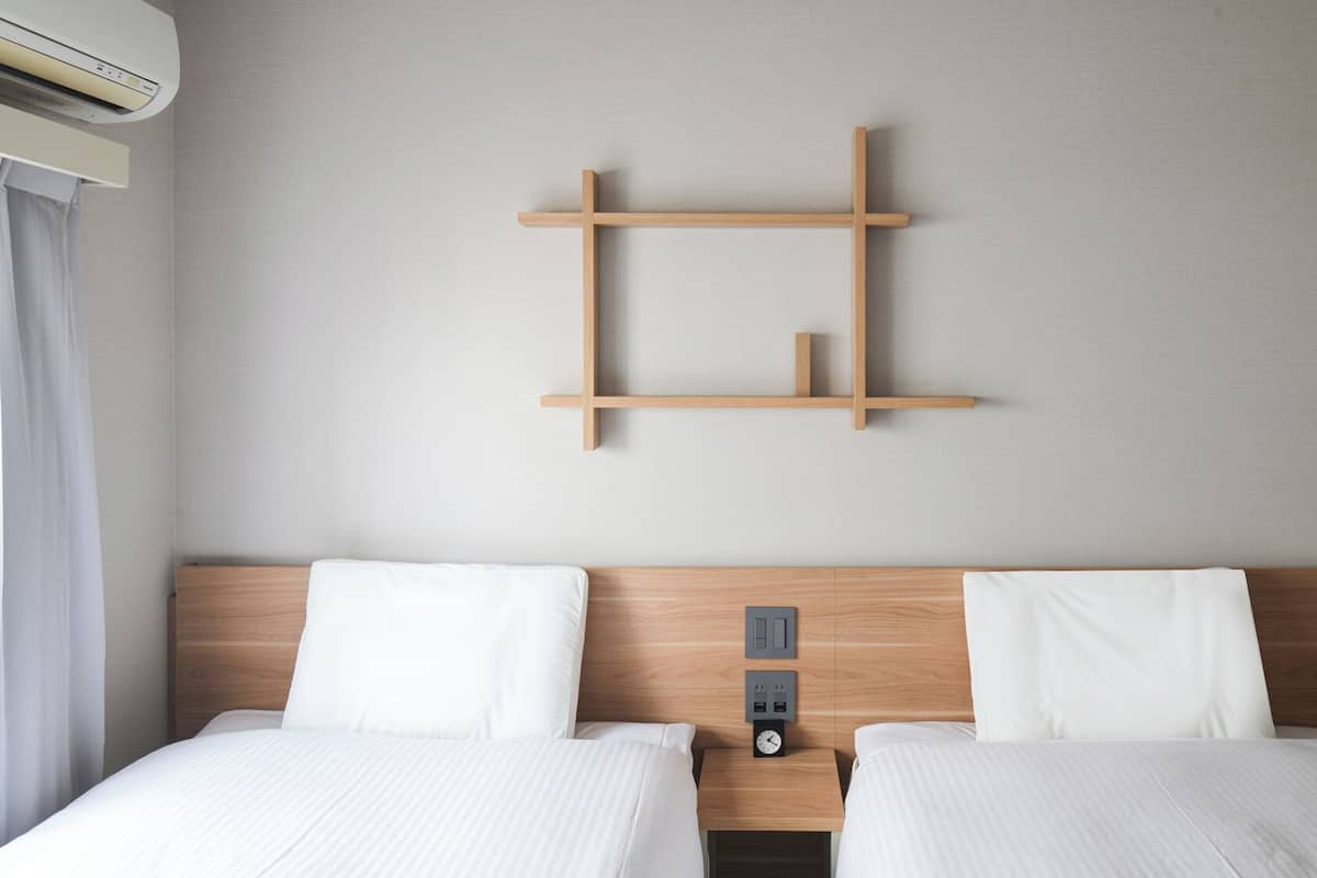 A hotel room with two beds, a wooden headboard, a wall-mounted shelf, and a wall-mounted air conditioning unit.