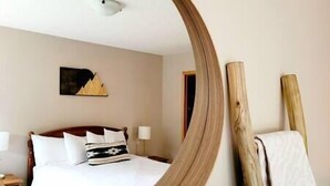 Una camera d'albergo con un letto, un comodino, una lampada, un quadro appeso e una struttura in legno appoggiata al muro.