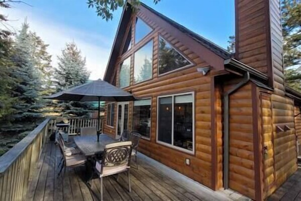 A wooden cabin with a deck, a table, and chairs.