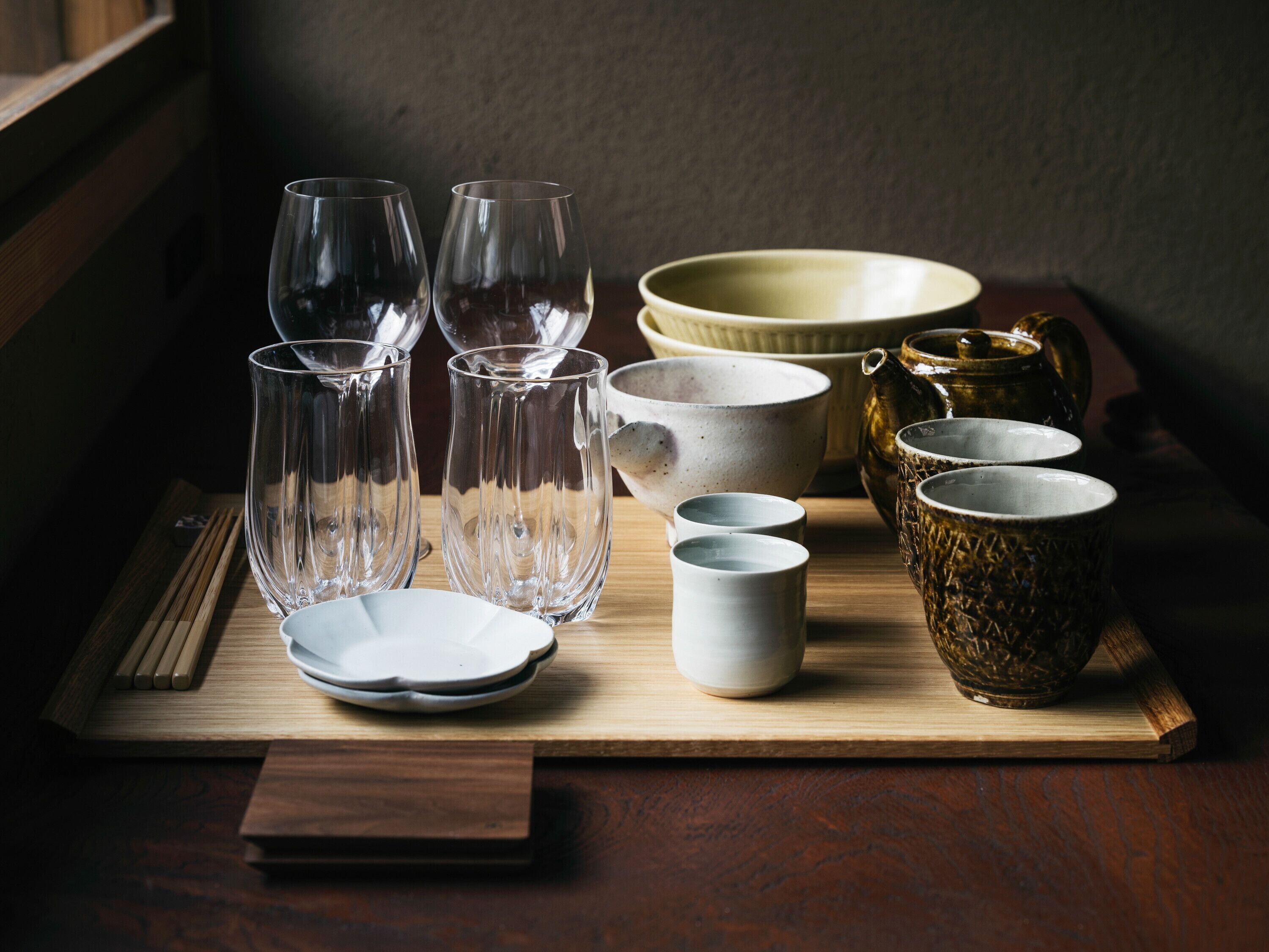 A wooden table with various glassware and ceramic items, including clear glasses, bowls, and a teapot.