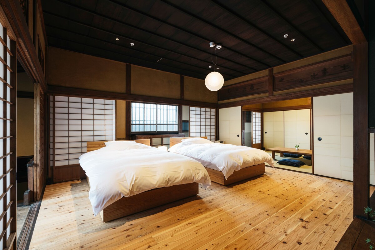 A traditional Japanese-style bedroom with two beds, wooden flooring, sliding doors, and a hanging light fixture.