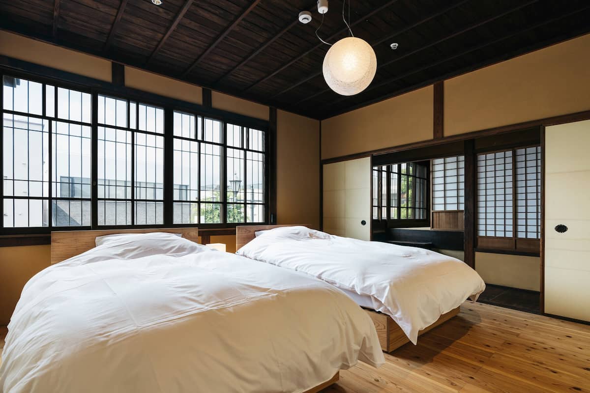 A room with two beds, large windows, and a wooden ceiling.