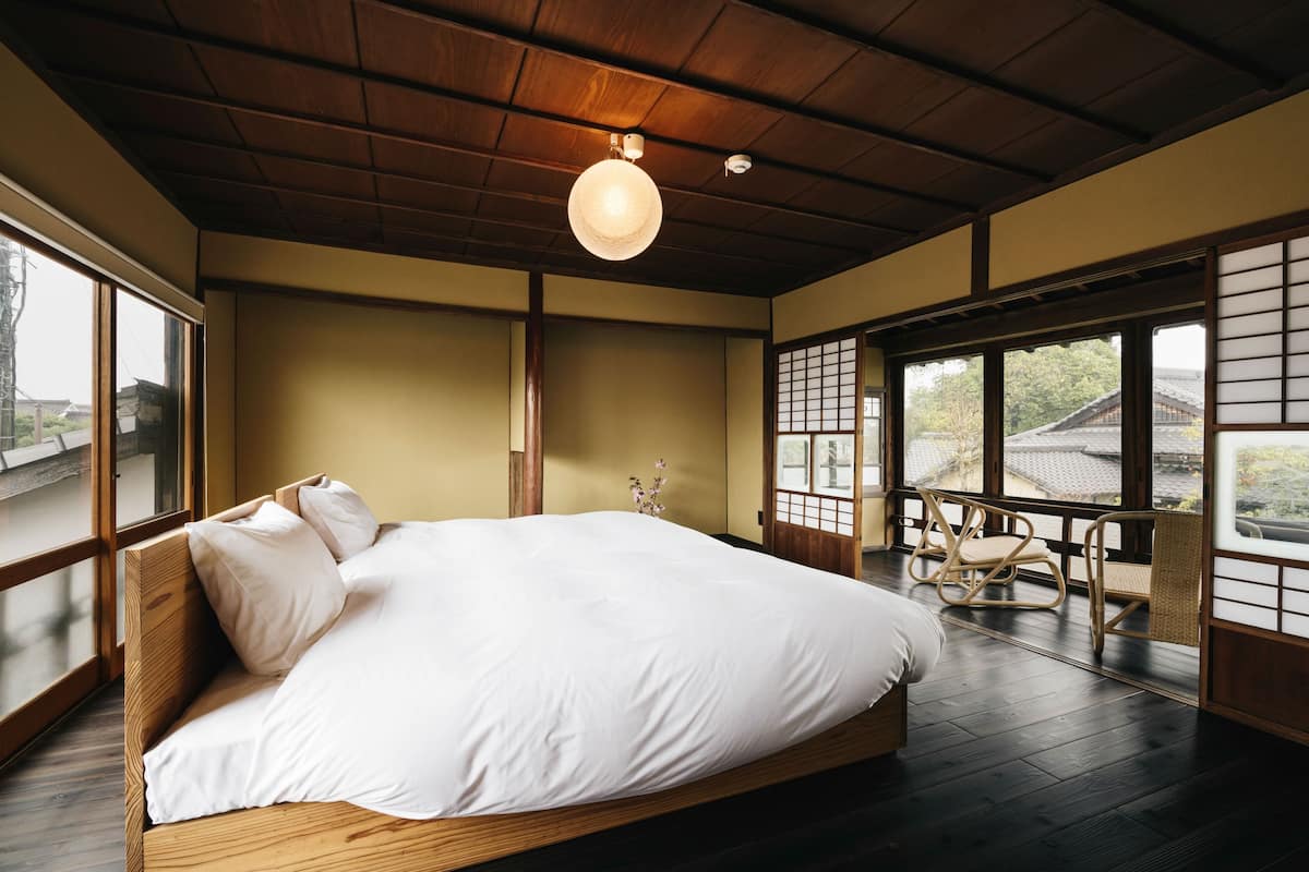 Ein traditioneller japanischer Raum mit Tatami-Boden, einem großen Bett mit weißer Bettwäsche, einer hängenden Leuchte und verschiebbaren Shoji-Türen.