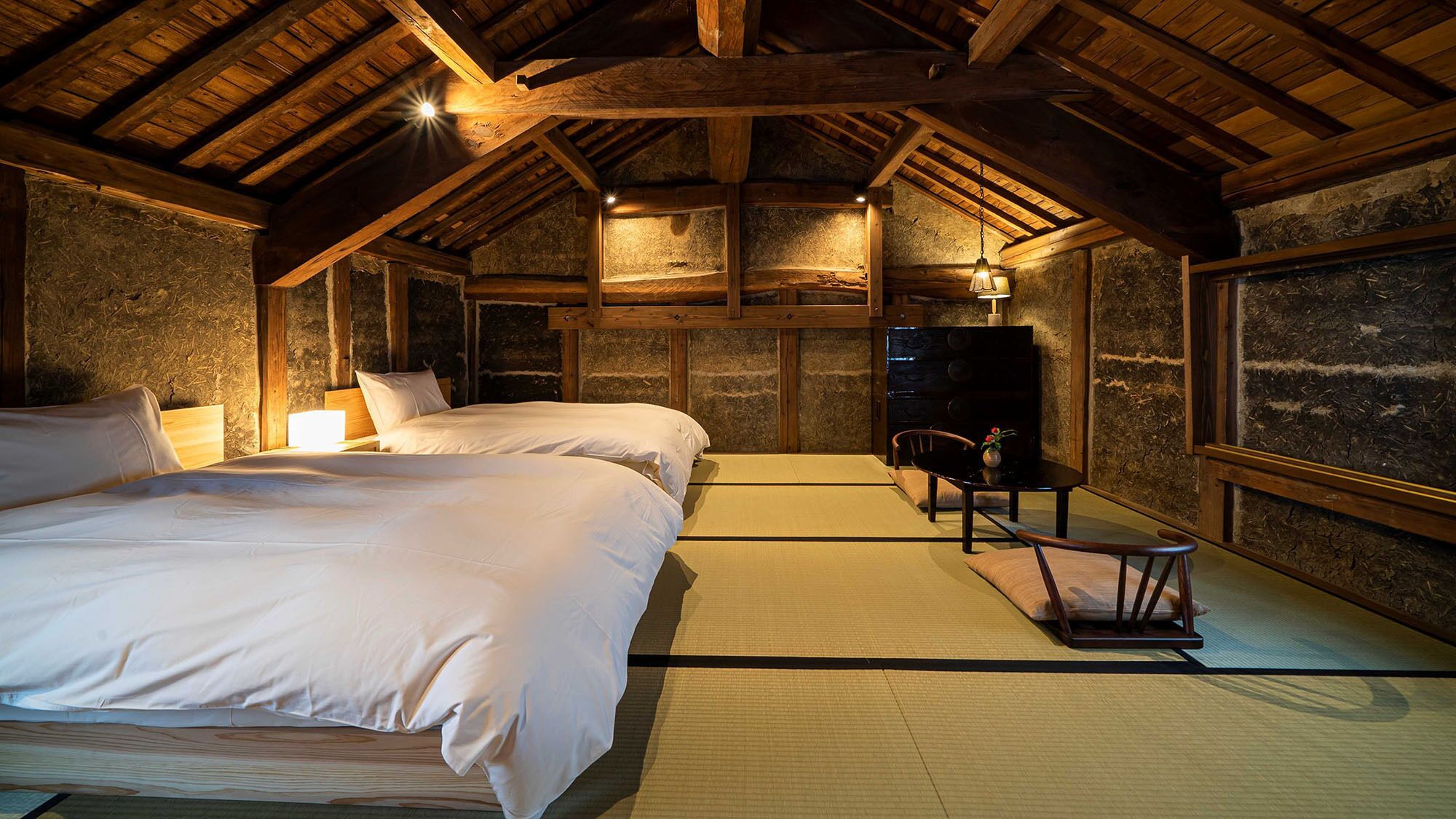 A traditional Japanese-style room with tatami flooring, two beds, a desk, and a television.
