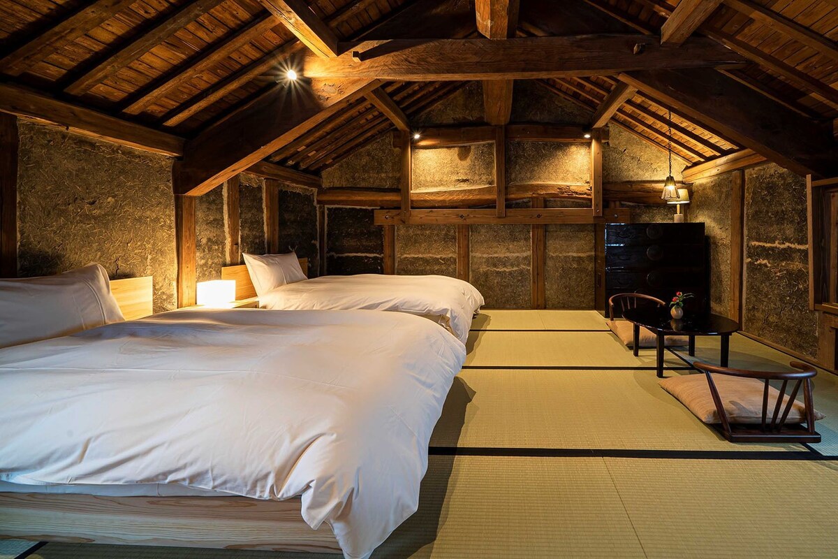 A traditional Japanese-style room with tatami flooring, two beds, a desk, and a television.