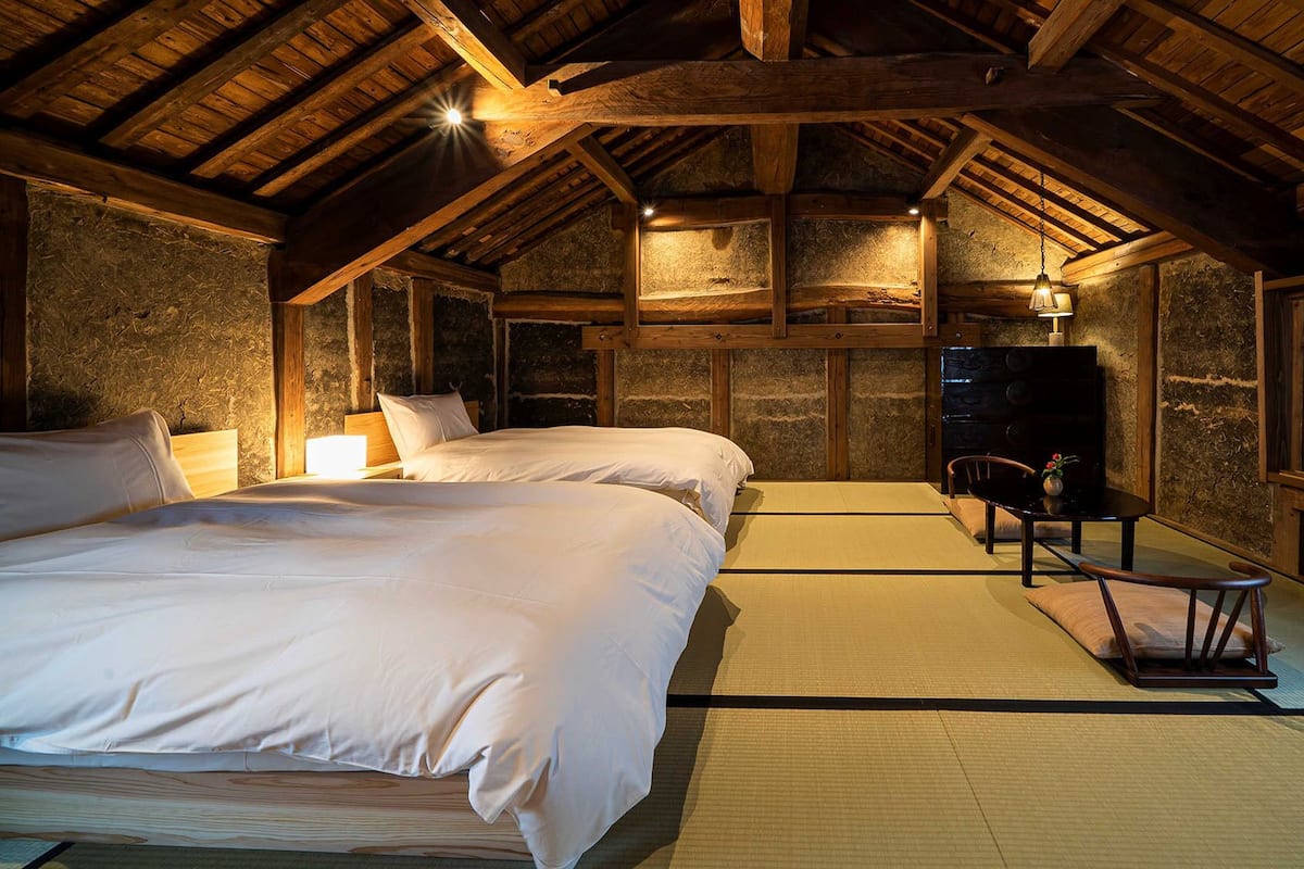 Ein traditioneller japanischer Raum mit Tatami-Boden, zwei Betten, einem Schreibtisch und einem Fernseher.