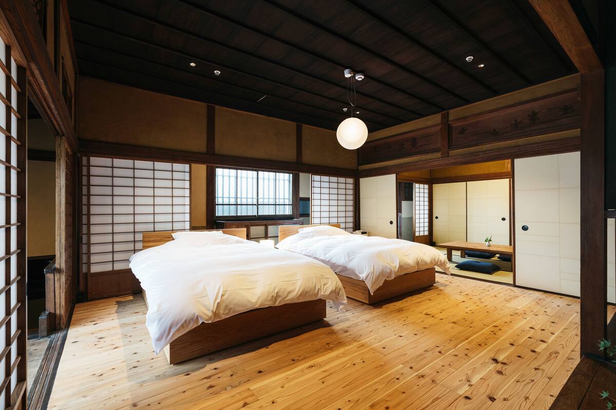 A traditional Japanese-style bedroom with two wooden beds, tatami flooring, sliding shoji doors, and a hanging light fixture.