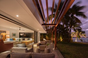 Un espace de vie extérieur doté d’une terrasse moderne, d’un coin salon et offrant une vue sur l’océan au crépuscule.