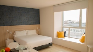 A modern hotel room with a bed, a dining area with a table set for two, and a large window with a city view. - Select Porto Suites (Porto)