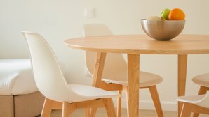 A round wooden dining table with a metal bowl containing fruits, surrounded by white chairs. - Select Porto Suites (Porto)