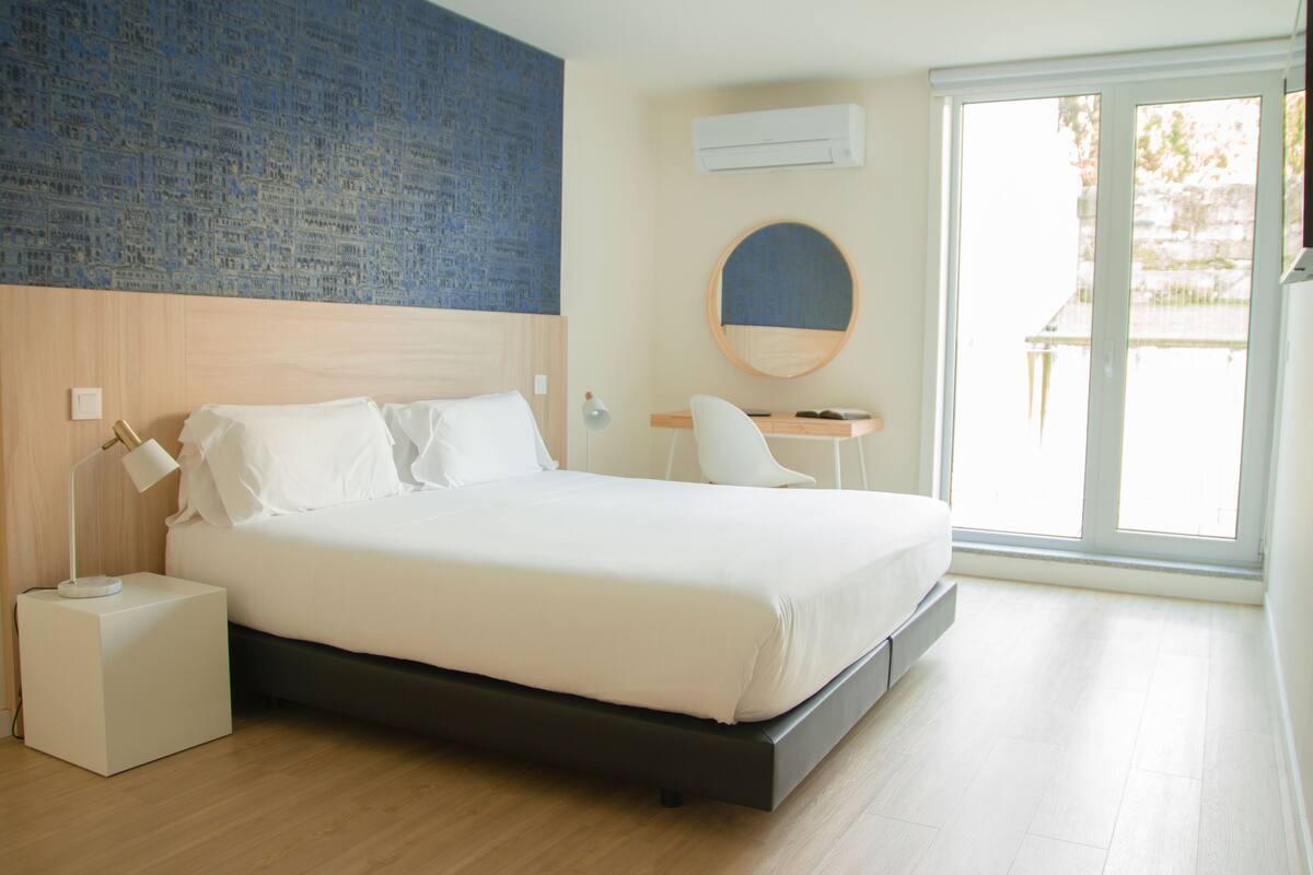 A modern bedroom with a bed, bedside table, lamp, and a round mirror.