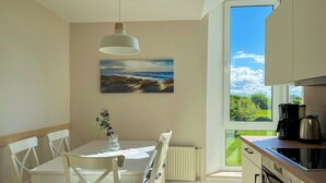 A modern kitchen with a dining area, a large window with a view, and a painting on the wall.