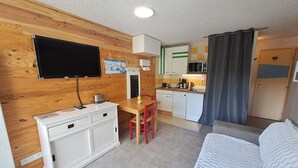 A compact room with a bed, a desk with a chair, a kitchenette, and a television mounted on the wall.
