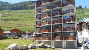 A multi-story hotel with balconies, a parking area, and a hilly landscape in the background.