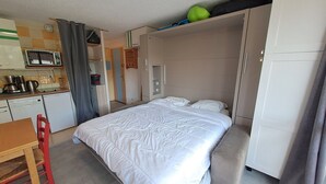 A compact room with a bed, a small kitchenette, a dining area, and a wardrobe.