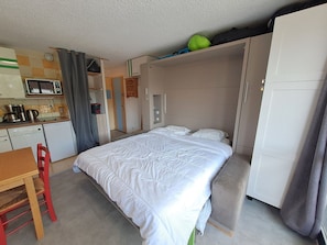 Una habitación compacta con cama, kitchenette pequeño, zona de comedor y armario.