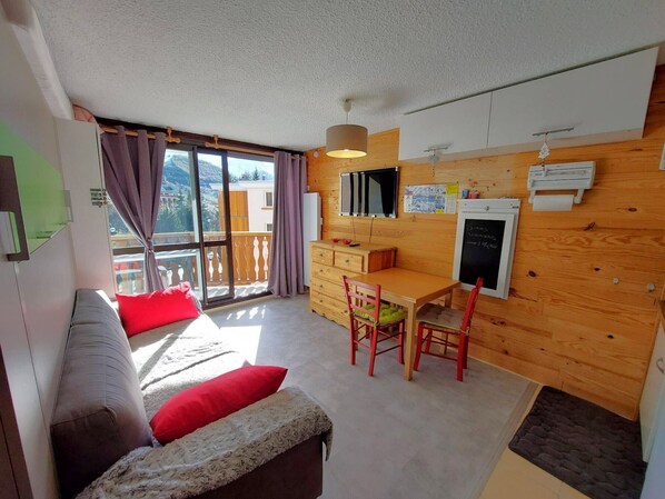 A room with a bed, a desk, a chair, a dresser, a window with curtains, and a view of the outside. - Modern studio, central, south-facing balcony, pets allowed (Les Deux Alpes)