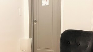 A grey door with a sign indicating room number 4, a black upholstered chair, and a clear plastic waste bin. - APARTMENT 4 PANTHEON (Roma)