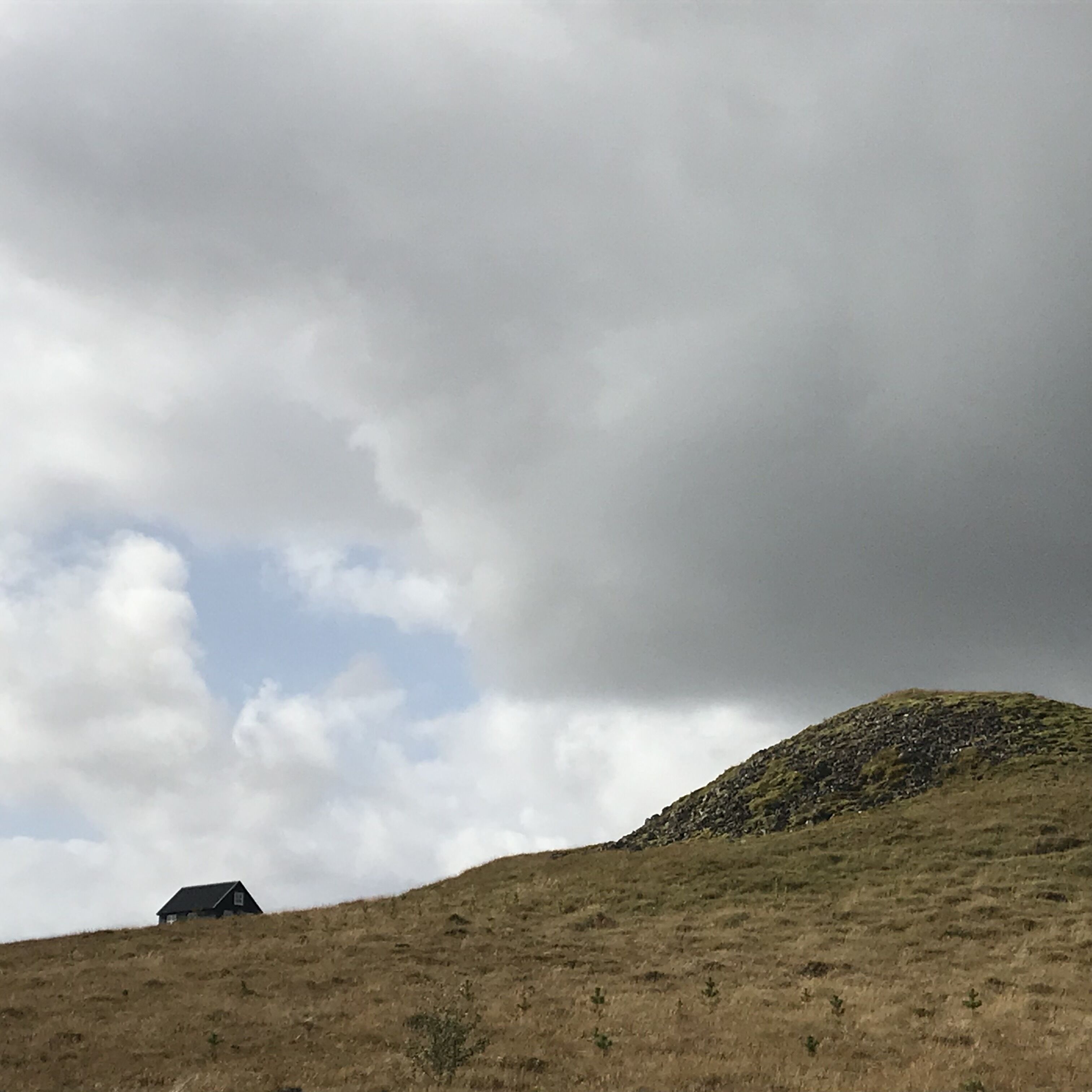 A grassy hill with a small house at the base.