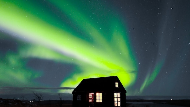 Una casa de exterior oscuro y con amplias ventanas, con la aurora boreal como telón de fondo.