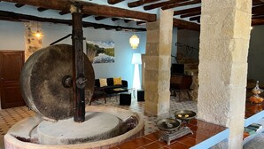 Un interior rústico con vigas de madera a la vista, un molino de piedra y suelo de baldosas.