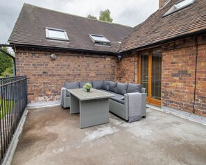 A brick building with a patio area featuring a grey sofa, a table, and a potted plant. - Jackfield Old School (Jackfield)