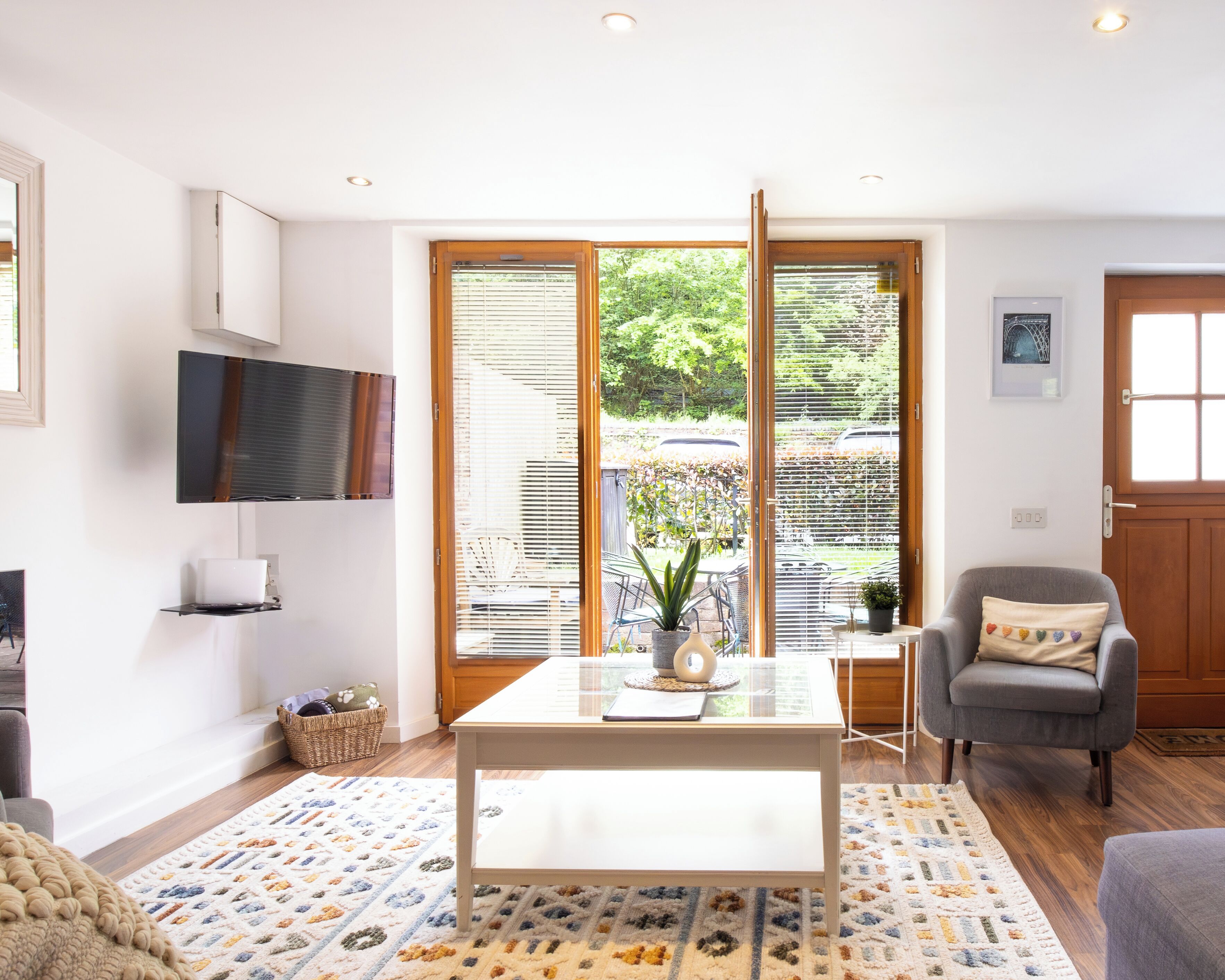 Una sala de estar moderna con televisor de pantalla plana, una mesa de centro, un sillón gris y vistas amplias por grandes ventanales.