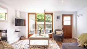 A living room with a sofa, a coffee table, a TV, and a door leading to a garden. - Jackfield Old School (Jackfield)