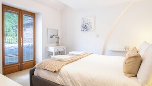 A bedroom with a bed, a desk, a chair, a window with blinds, and a door. - Jackfield Old School (Jackfield)