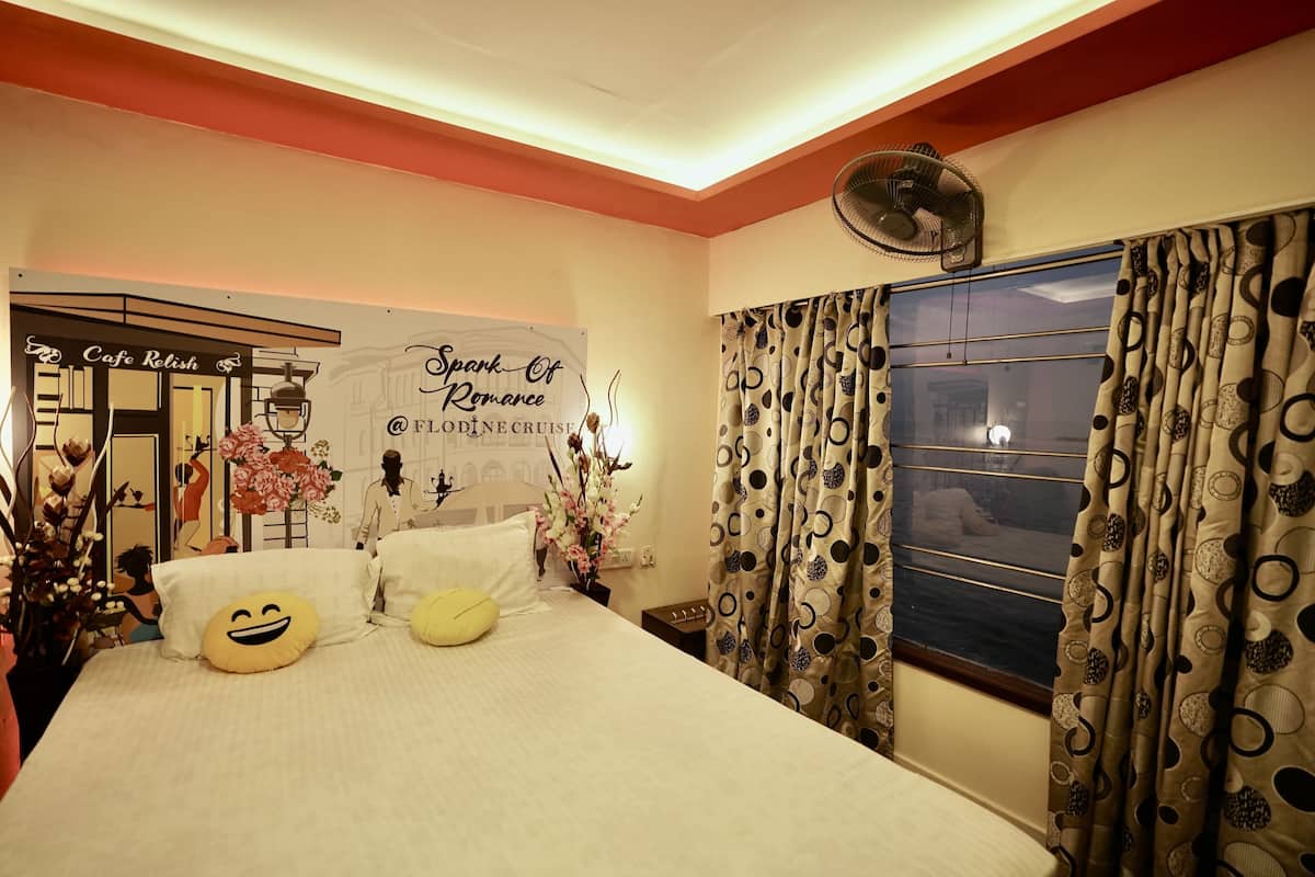 A hotel room with a bed, pillows, a fan, curtains, and a wall with a sign.