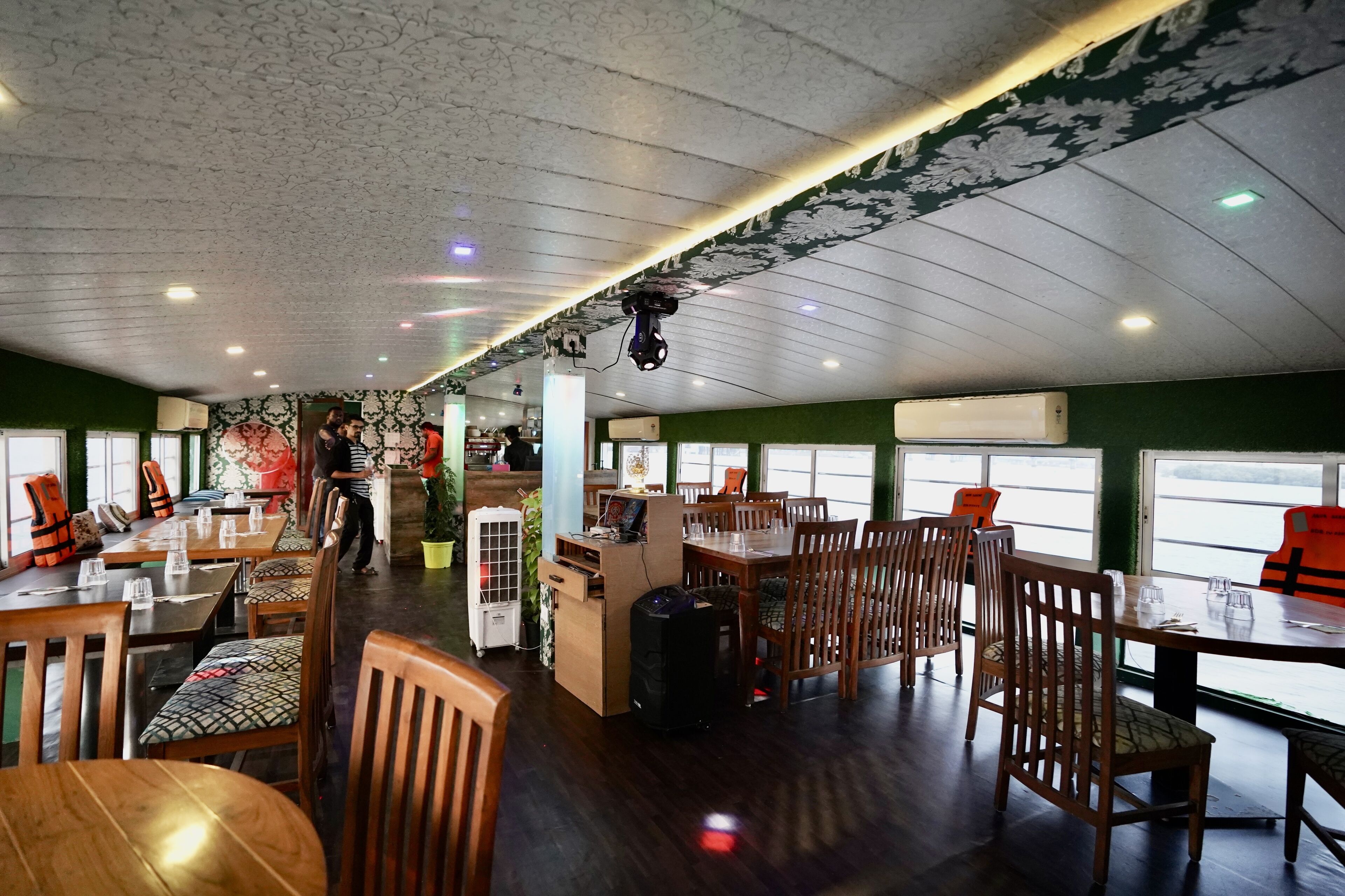 A spacious restaurant with wooden tables and chairs, a counter, and large windows offering views.