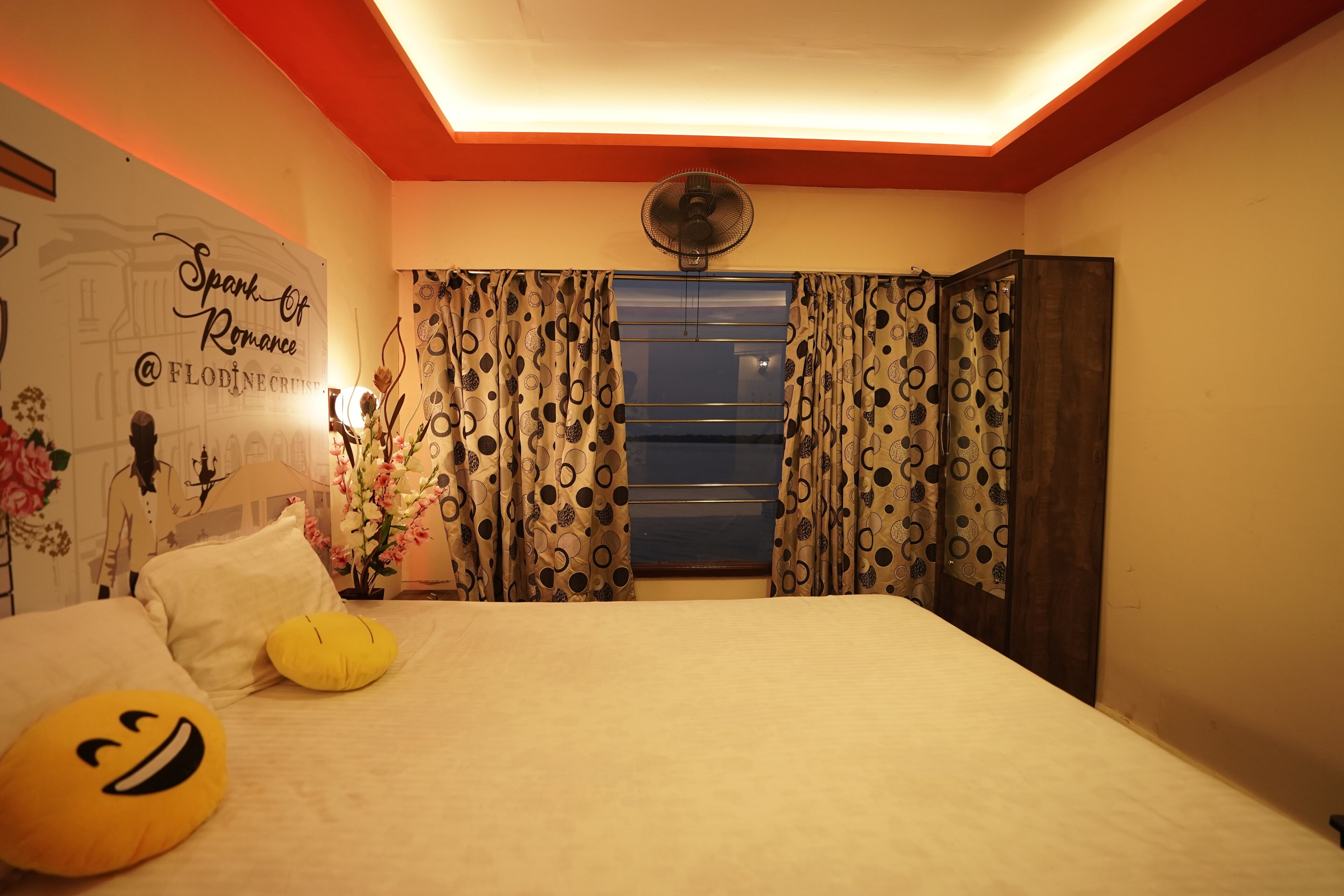 Un dormitorio con cama, almohadas, cortinas, un ventilador y una pared con un cartel.