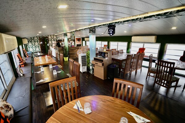 A restaurant with wooden tables and chairs, a stage with a microphone, and a large window.