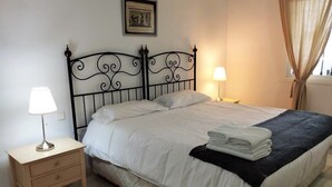 Un letto ben rifatto con una testiera nera, un comodino con una lampada e un asciugamano piegato sul letto.
