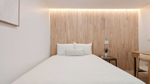Ein schlicht eingerichtetes Schlafzimmer mit einem hölzernen Kopfteil, einem Bett mit weißer Bettwäsche und einem kleinen Nachttisch mit einer Vase.