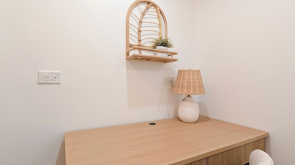 A bathroom with a wooden vanity, a wall-mounted shelf with a plant, a lamp, and a power outlet.