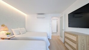 Habitación de hotel con dos camas, un televisor, una mesita de noche con lámpara y un aparador de madera.